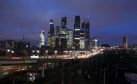 City landscape with many railroad tracks going far, cars on the overpass and skyscrapers with towers...