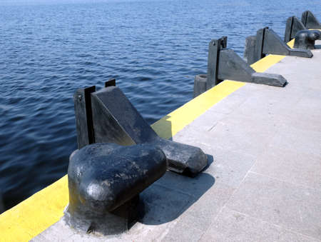 Black heavy bollards on empty pier edge on seaside diagonal view on sunny day