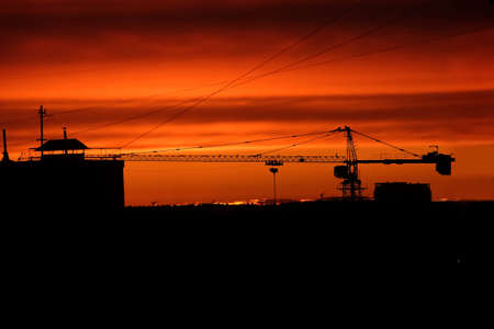 Industrial landscape with black silhouettes of construction crane and top of the building before fire sunset with red skies at the end of the dayの写真素材