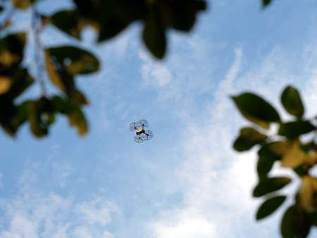 Four engine drone with engine protection grid flying high in the blue sky with calm white clouds...