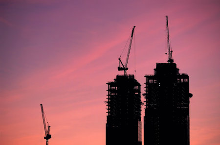 Contours of tower cranes above the high constructing tower buildings against evening sky in the red beautiful sunsetの写真素材
