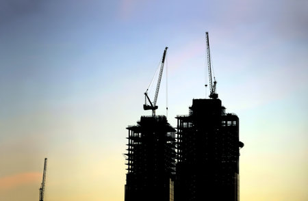 Contours of tower cranes above the high constructing tower buildings against early morning sky in the beautiful sunriseの写真素材