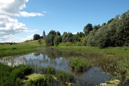 Beautiful hush rural landscape with still pond on front, old church and clouds on the sky in bright summer dayの写真素材