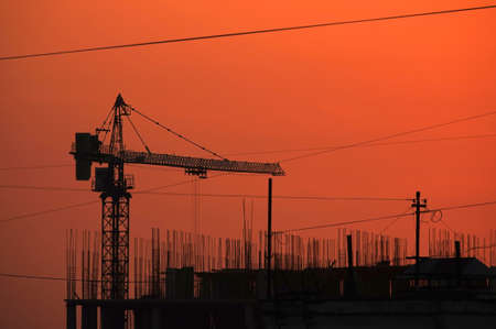 Contour of tower crane above the constructing buildings against clear evening sky on the red beautiful sunsetの写真素材