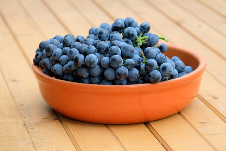 Lot of ripe red grape berries on bunch in brown round bowl on wooden table front view close-upの写真素材