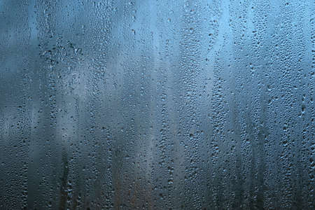 Background with rain droplets on window glass on gloomy autumn day on blur blue background close upの写真素材