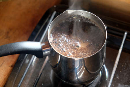Tasty flavored coffee with foam preparing in metal cezve on a gas stove in a house kitchen top view photo close upの写真素材