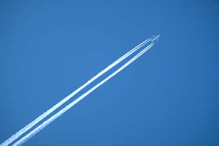 Large four engine passenger supersonic aircraft flying from left to right high in clear blue cloudless sky leaving bright long white trailの写真素材