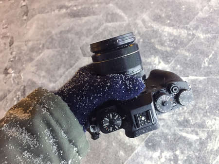 Top view of modern digital black color camera with lens in photographer's left hand worn in green jacket and blue wool glove in the extreme weather conditions in winter dayの写真素材