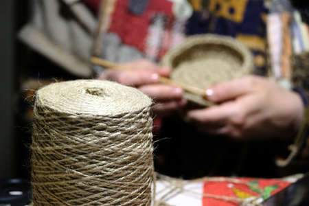 Woman in national rural clothes knits household items from a rope with big reel rope close-up on frontの写真素材