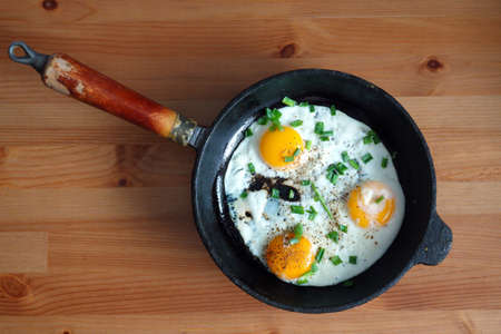 Fried eggs of three eggs on an old cast-iron frying pan standing on brown wooden table top view closeupの写真素材