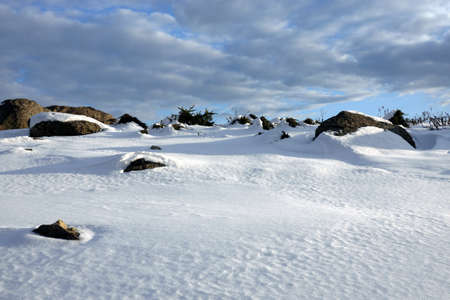 Winter tundra landscape with hilly snowy surface with stones and large boulders and long shadows from them under a beautiful blue sky with cloudsの写真素材