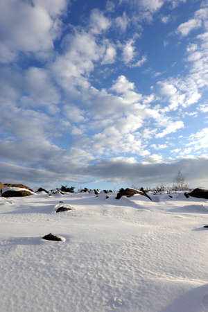 Winter tundra landscape with hilly snowy surface with stones and large boulders and long shadows from them under a beautiful blue sky with cloudsの写真素材