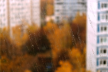 Landscape with autumn in the city view through transparent window glass with focus on rain dropletsの写真素材