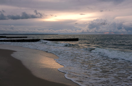View to wonderful landscape on Baltic Sea with sea waves, piers and beautiful heavy colorful clouds on skyline on colorful sunsetの写真素材