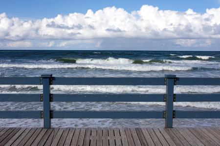 View to the sea waves under blu sky with dense clouds on skyline from pier with blue wooden fence on bright sunny windy dayの写真素材