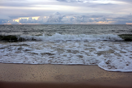 Landscape overlooking the sea in the evening with stormy clouds at far and sea waves washing the sand beachの写真素材
