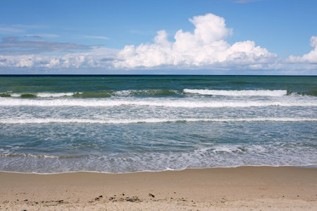 Beautiful seaside landscape with calm sea surf with emerald waves runs to the empty sandy beach and white clouds on skyline in bright sunny dayの写真素材