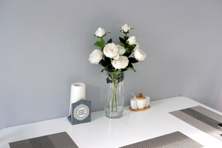 Modern stylish interior of dining room in soft pastel colors with white furniture and rose bouquet in vase on the tableの写真素材