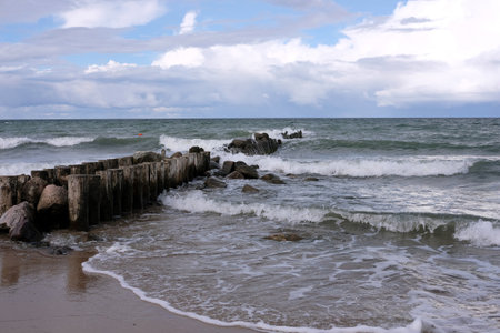 Seaside landscape with wooden logs as wavebreaker going far in the stormy sea under gray heavy rain clouds in windy dayの写真素材