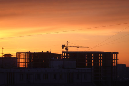 Contour of tower crane above the constructing buildings against cloudless evening sky on the red sunset on the end of workind dayの写真素材