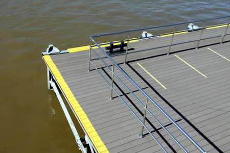Part of the jetty with yellow marking and metal handrail fencing with handrails near the water surface on a clear sunny dayの写真素材