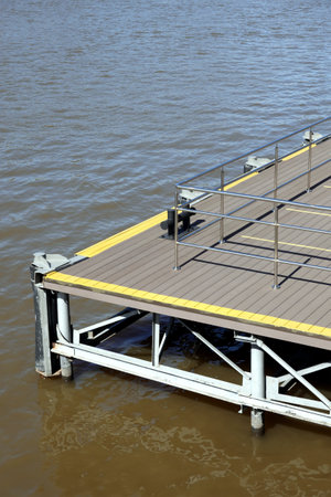 Part of the jetty with yellow marking and metal handrail fencing with handrails near the water surface on a clear sunny dayの写真素材