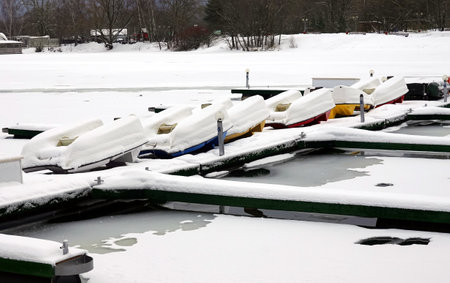 WInter landscape with many overturned boats covered with snow on a dock on a frozen river in no seasonの写真素材