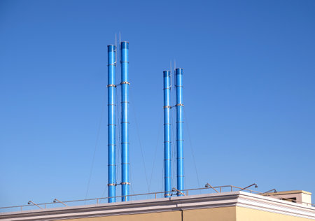 Four painted blue smoke stacks after roof of building on clear blue sky without cloudsの写真素材
