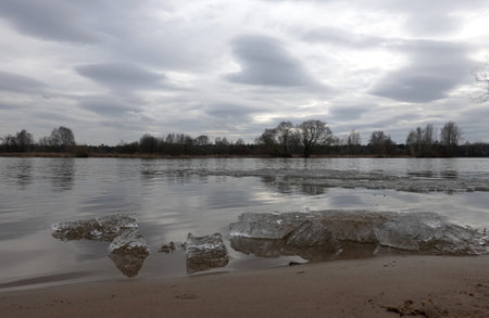 Landscape with last broken ice near the river shore under heavy clouds on overcast spring eveningの写真素材