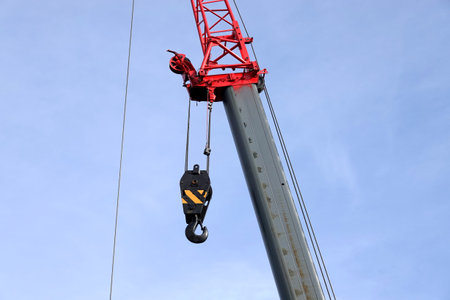 Big heavy hook with yellow stripes on metal cable on construction arm crane with red top closeup viewの写真素材