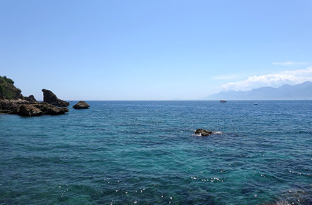 Beautiful calm sea and rocks in front and high mountains in haze at far in sunny summer dayの写真素材