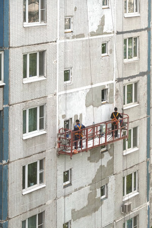 Two workers in construction cradle on metal cables repairing wall surface on block of flats house on the highの写真素材