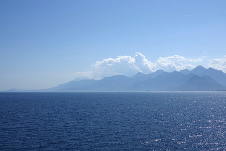 Beautiful mediterranean landscape in soft colors with calm sea and high mountains silhouettes covered with light haze on skylineの写真素材