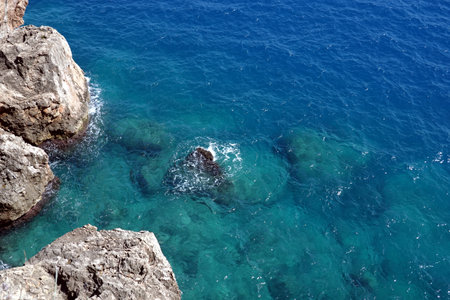 View from high rocky shore to the azure transparent sea water with foam in bright sunny dayの写真素材