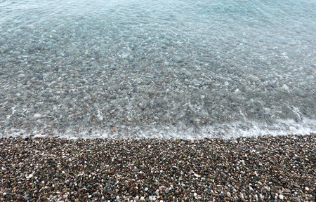 Beach with many small smooth pebble and clean calm transparent sea and light surfの写真素材