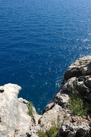 View from high rocky shore to the azure transparent sea water with sunlight reflection in bright...