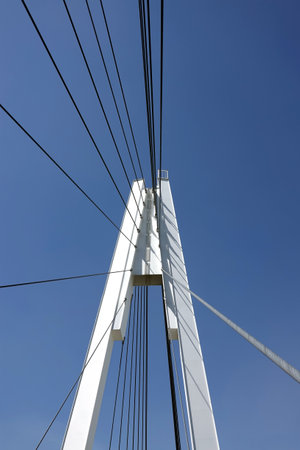 Modern urban cable-stayed bridge with metal ropes over cloudless blue skyの写真素材