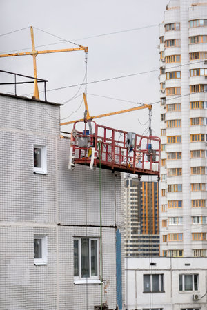 Empty construction cradle on metal cables on the high while pause in repairing wall surface on block of flats houseの写真素材