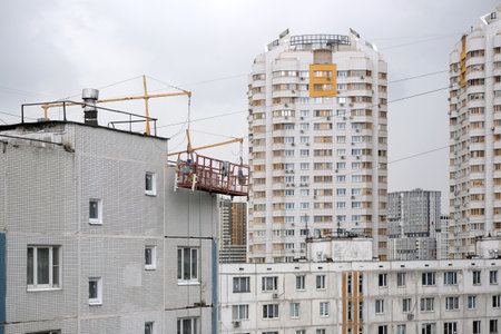 Break during work. Empty construction cradle on metal cables on the high near the wall surface on block of flats houseの写真素材