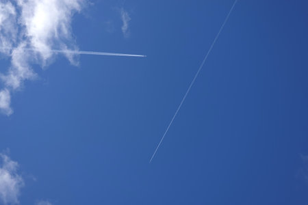 Two aircrafts flying high with long white trails in blue skyの写真素材