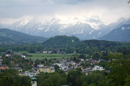 Beautiful natural landscape with high inaccessible snow mountains and alpine forests at far in the clouds after town houses in the valleyの写真素材