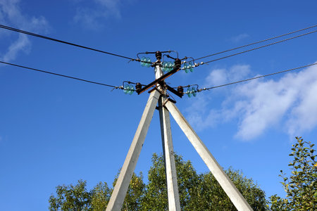 Top of pylon of power supply line with wires and insulators in rural place under blue sky with white cloudsの写真素材
