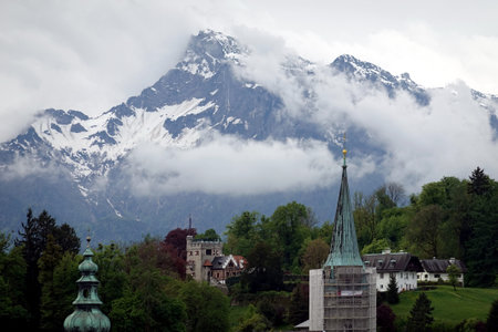 Beautiful landscape with high inaccessible snow mountains and alpine forests in the fog at far after Salzburg houses roofs and steeplesの写真素材