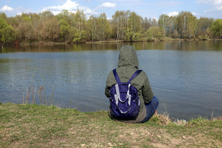 Lonely woman sitting and rests on the high river coast in spring day view from the backの写真素材