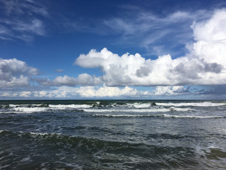 Contrast Seascape with stormy sea waves with foam under heavy cumulonimbus on blue sky till horizonの写真素材