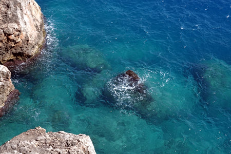 Top view from high rocky shore to the azure transparent sea water with foam in bright sunny dayの写真素材