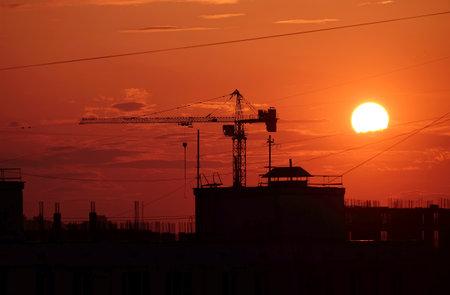 Contour of tower crane above the constructing buildings against evening sky with beautiful red sunset and yellow sunの写真素材