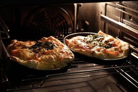 Two big homemade prepared pizza with bacon tomatoes and cheese inside the kitchen stove front view close upの写真素材
