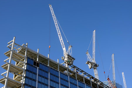 Strong hoisting tower crane on the top section being construction of modern high skyscraper building against blue cloudless skyの写真素材
